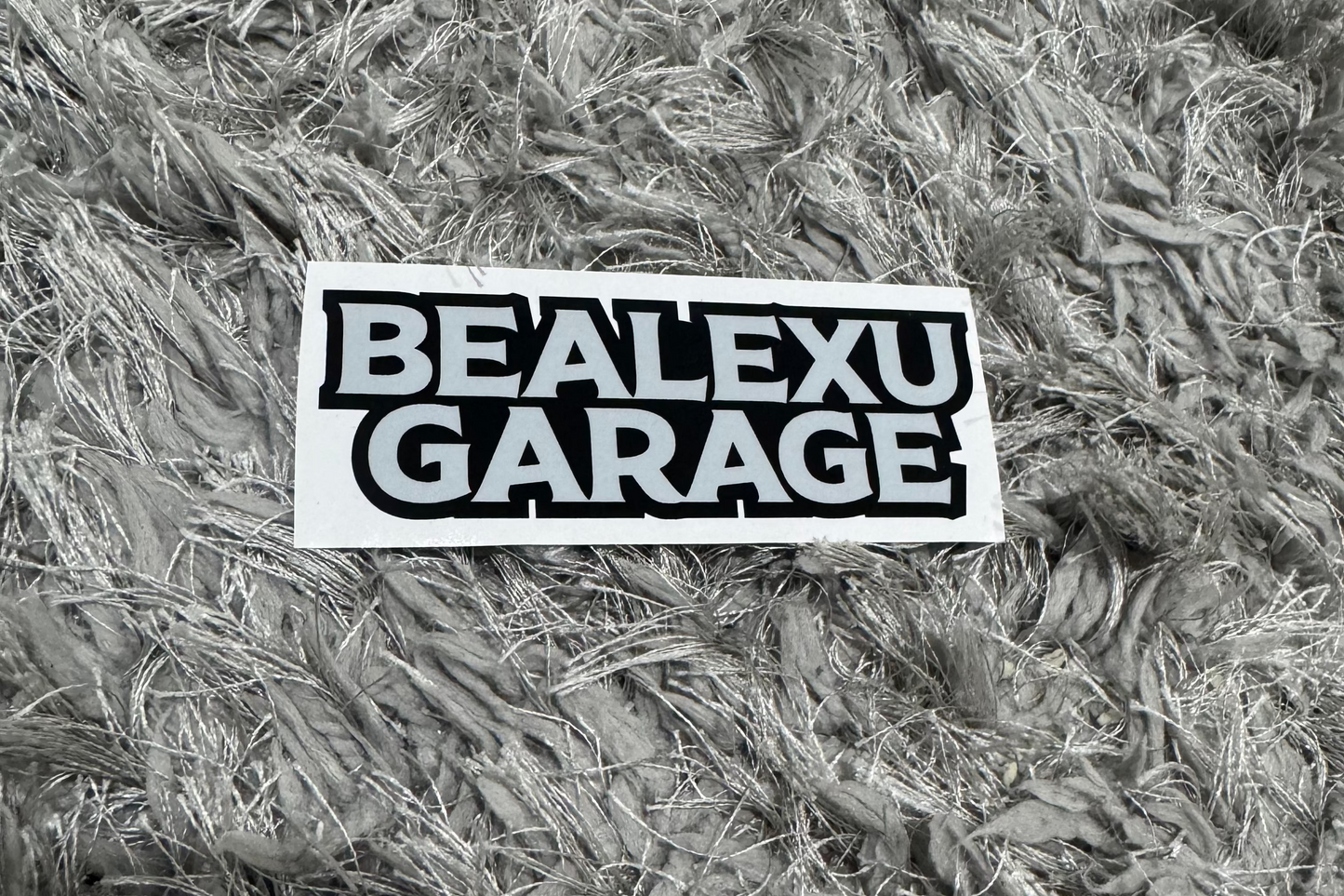 Sticker with 'BEALEXU GARAGE' text on a textured surface